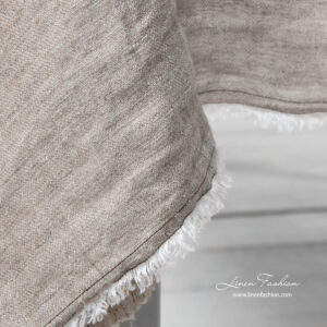 Light grey tablecloth's edge with brown stitches and fringe