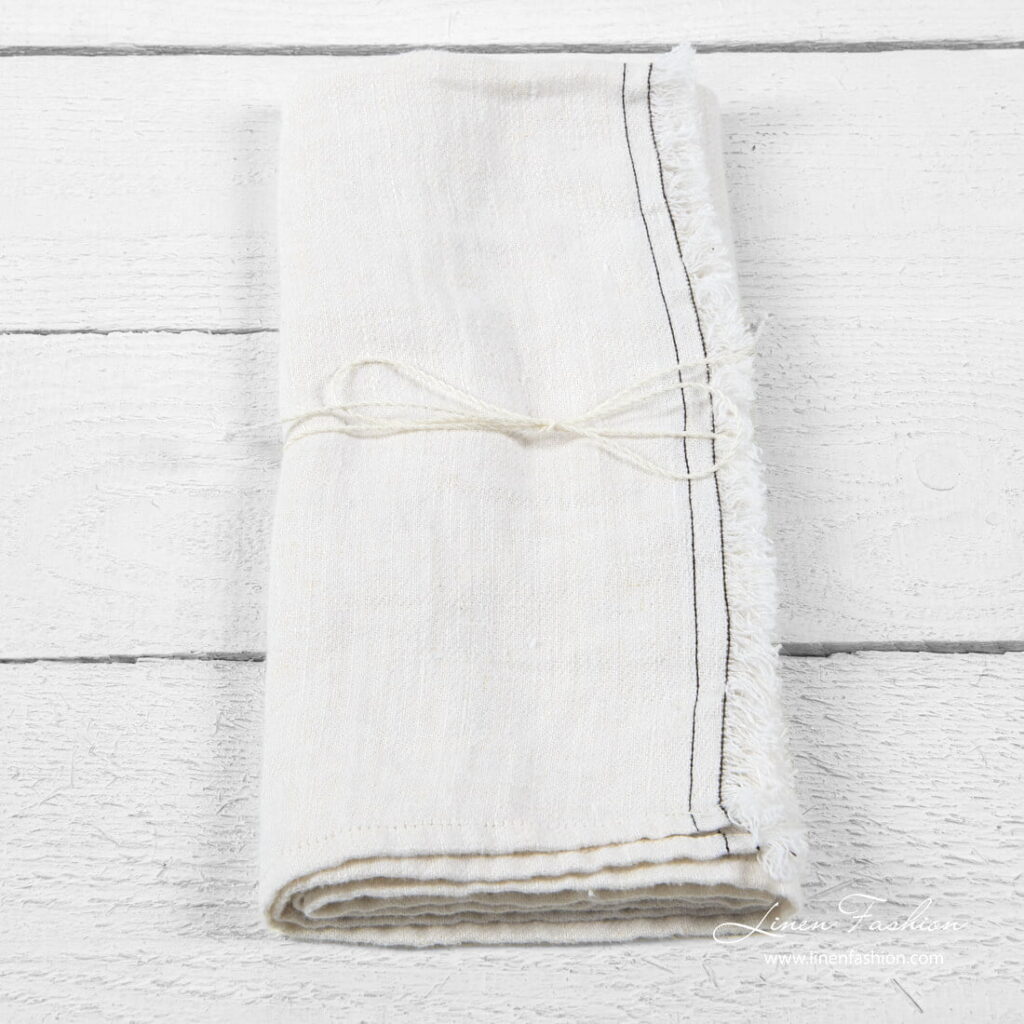 White kitchen towel with brown stitches and loose fringes on one side